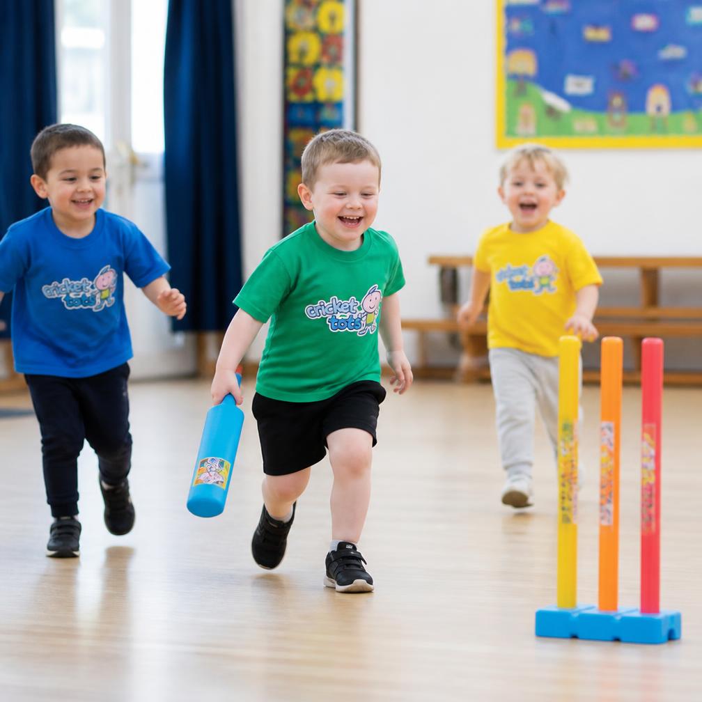 Toddlers running towards colourful cricket stumps in a school hall